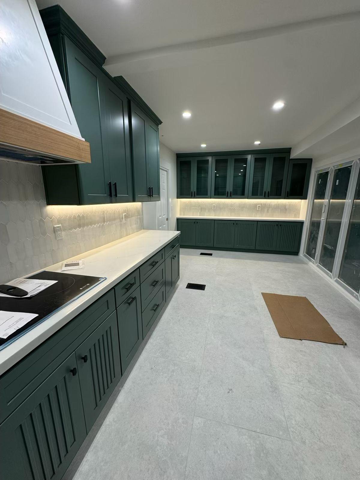 The finished galley kitchen: deep green cabinetry under a white oak banded hood, quartz countertops and glass-front cabinets