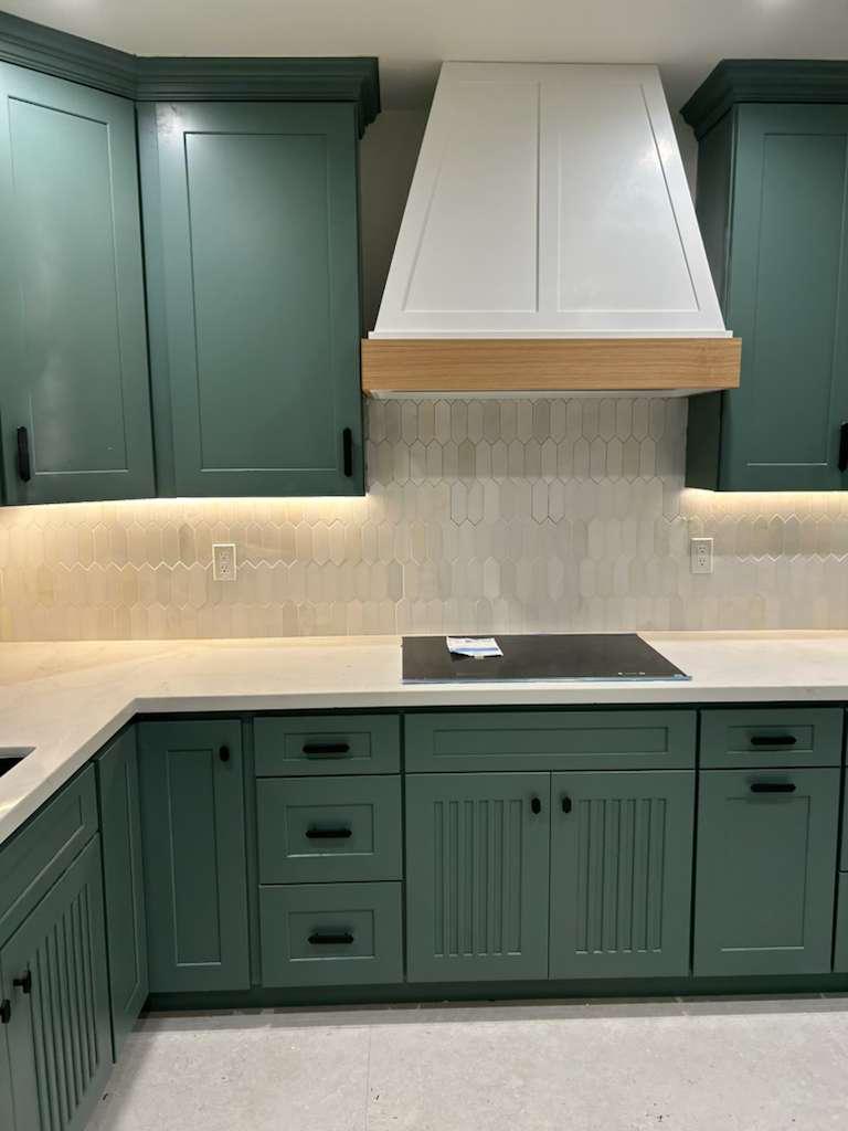 Cooking wall elevation: the white oak banded hood centered over the cooktop between tall green cabinets